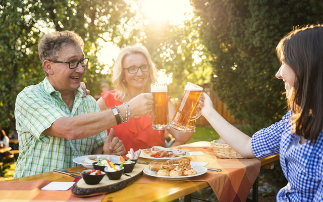Personen stoßen im Freien mit Biergläsern an, Essen auf dem Tisch.