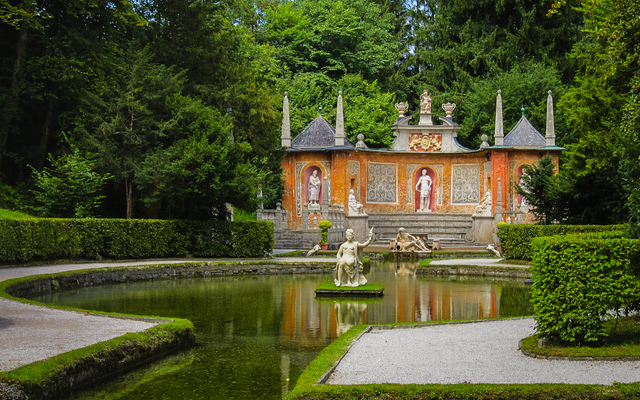 Teich im Schloss Hellbrunn in Salzburg, umgeben von üppiger Vegetation und dekorativen Elementen.