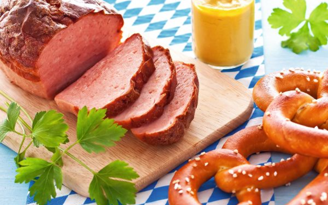 Leberkäse auf Holzbrett mit Brezeln und Senf auf bayerischer Tischdecke