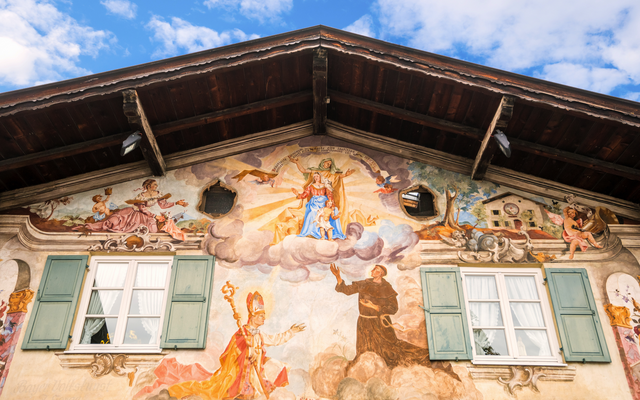 Bemaltes Haus mit religiösen Motiven, grünen Fensterläden und Holzdach.