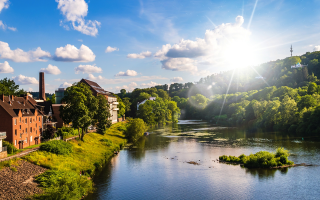 Fluss mit Bäumen und Gebäuden unter blauem Himmel bei Sonnenschein.