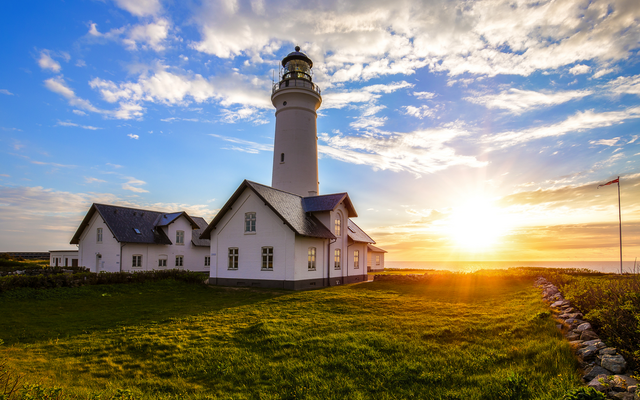 Leuchtturm und Gebäude bei Sonnenuntergang vor bewölktem Himmel