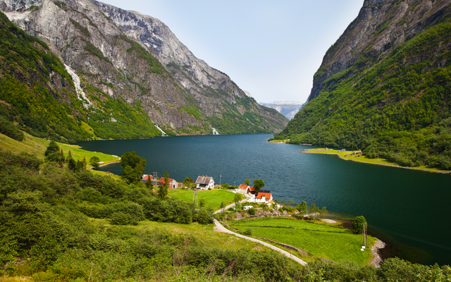 Blick auf malerische Fjordlandschaft mit Bergen und kleinen Häusern am Wasser.