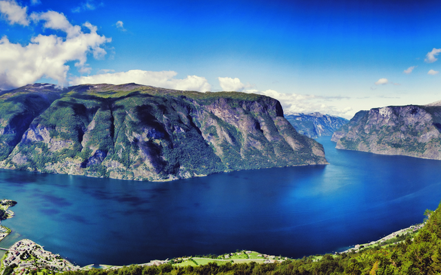 Panorama eines tiefen blauen Fjords, umgeben von bewaldeten Bergen und klarem Himmel.