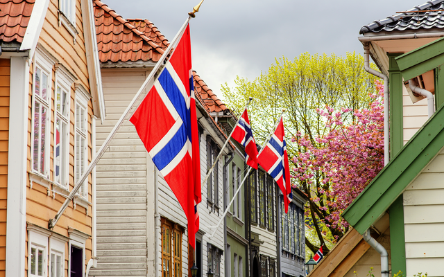 Norwegische Flaggen an bunten Häusern in einer Straße mit blühendem Baum.