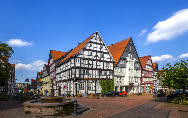 Historischer Marktplatz mit Fachwerkhäusern und Brunnen bei klarem Himmel.