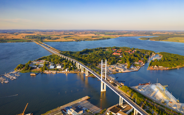 Luftaufnahme einer Brücke über einem Fluss mit Insel und Landschaft im Hintergrund.