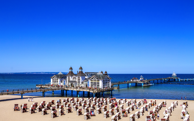 Seebrücke Sellin an einem sonnigen Tag, blauer Himmel, viele Strandkörbe im Vordergrund am Strand.