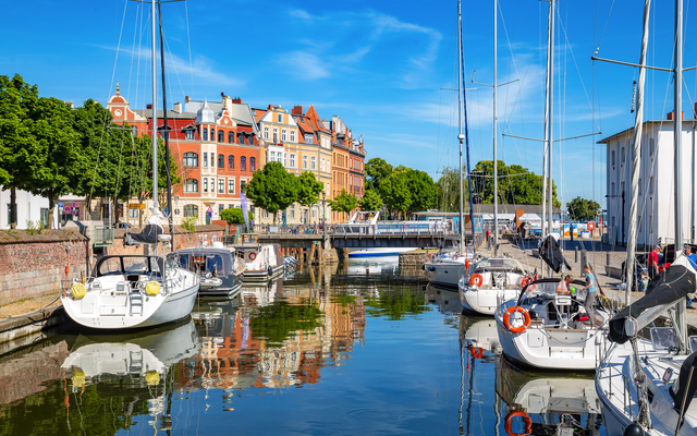 Segelboote im Hafen vor historischen Gebäuden bei klarem Himmel.