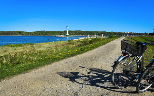 Fahrrad auf einem Weg am Wasser mit einem Leuchtturm im Hintergrund.
