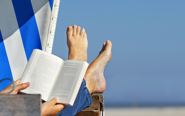 Person entspannt im Strandkorb mit einem Buch, Füße hochgelegt.