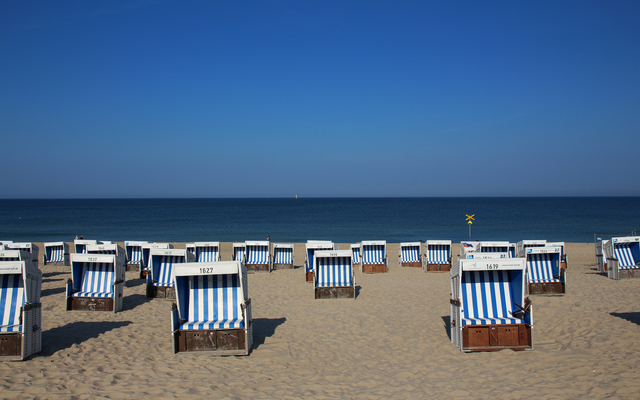 Strandkörbe am Sandstrand vor blauem Himmel und Meer.
