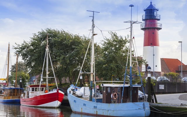 Fischkutter im Hafen von Büsum mit einem Leuchtturm im Hintergrund.