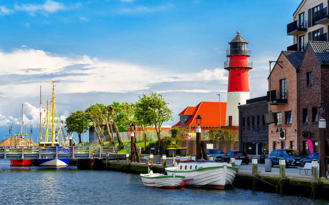 Küstenstadt mit Leuchtturm, Segelbooten und roten Backsteinhäusern am Wasser.