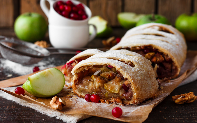 Apfelstrudel mit Nüssen, Preiselbeeren und Apfelscheiben auf Holztisch.