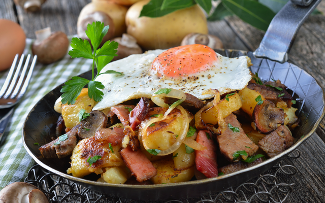 Bratpfanne mit Bratkartoffeln, Spiegelei, Speck und Zwiebeln, garniert mit Petersilie.