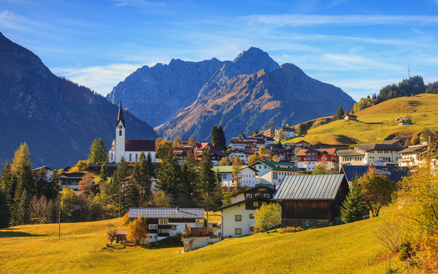 Bergdorf mit Kirche und Häusern, im Hintergrund Gebirge bei klarem Himmel.