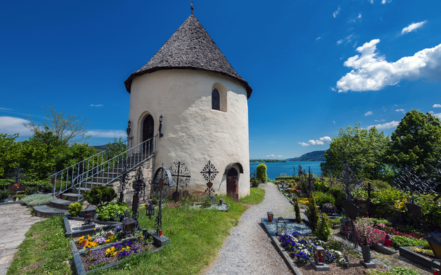 Rundkirche mit Friedhof vor blauen Himmel und See im Hintergrund.