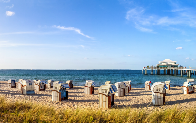 Panoramablick auf einen Strand mit Strandkörben und einer Seebrücke.