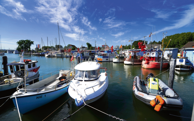 Boote in einem Hafen bei blauem Himmel und ruhigem Wasser.