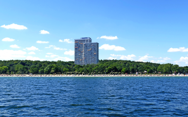 Ein hohes Gebäude an der Küste mit Wald und Strand im Vordergrund.