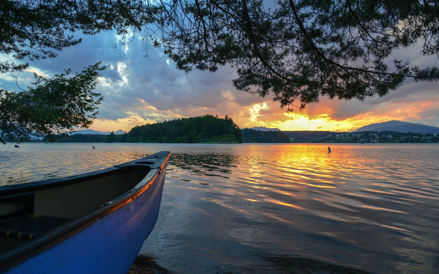 Kanu im See bei Sonnenuntergang mit Insel und bewölktem Himmel im Hintergrund.