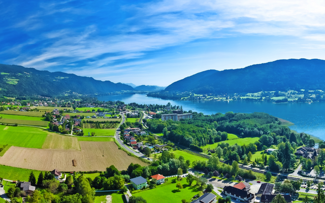 Panorama eines grünen Tals mit einem großen See und bewaldeten Bergen.