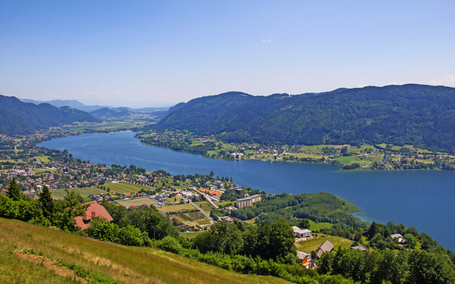 Blick auf einen großen, von Bergen umgebenen See mit Dörfern am Ufer.