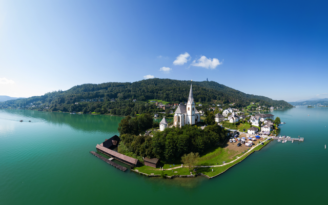 Luftaufnahme einer Kirche auf einer Halbinsel im See mit umliegender Landschaft und Bergen.