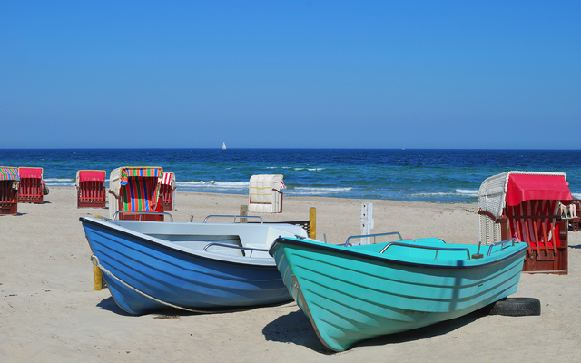 Zwei bunte Boote am Strand mit Strandkörben im Hintergrund.