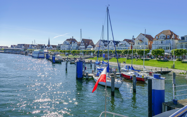 Hafen mit Segelbooten und Häusern im Hintergrund bei sonnigem Wetter.