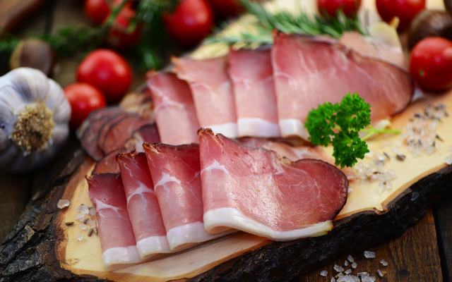 Aufgeschnittener Schinken auf Holzbrett mit Tomaten und Knoblauch