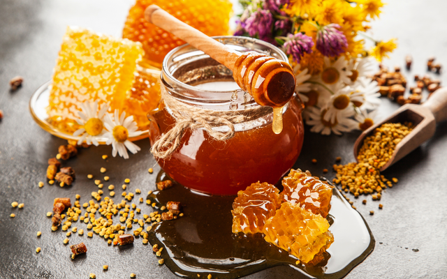Ein Glas Honig mit Holzlöffel und Bienenwabe auf einem Tisch.