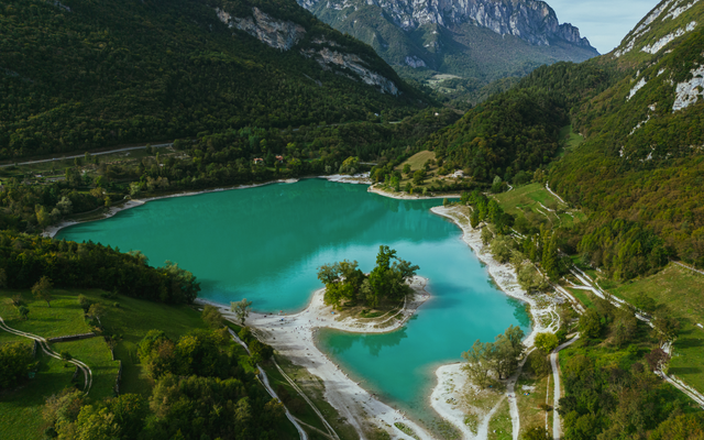 Bergsee mit türkisblauem Wasser, umgeben von grünen Bergen und Wäldern.