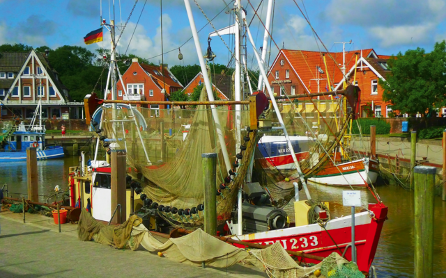 Fischkutter im Hafen von Neuharlingersiel mit roten Häusern im Hintergrund.