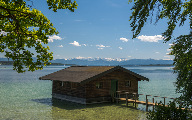 Holzhütte auf einem See mit Berglandschaft im Hintergrund.