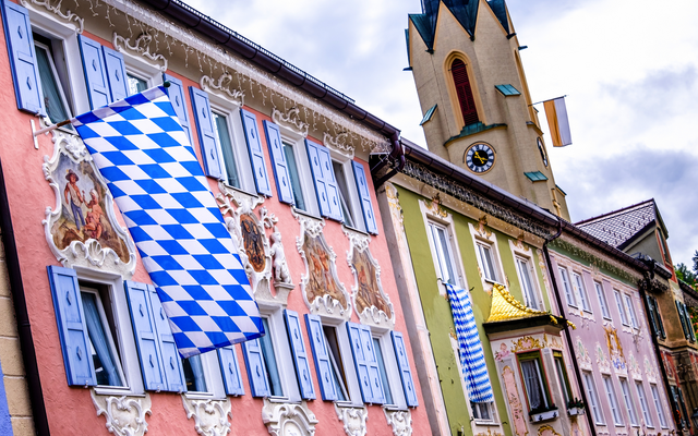 Bunte Gebäude mit bayerischen Fahnen und Kirchturm im Hintergrund.