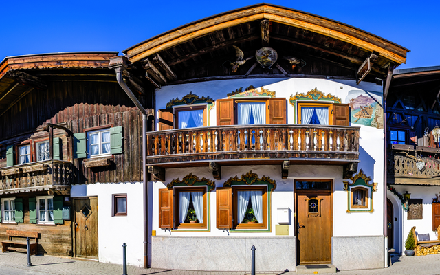 Traditionelle bayerische Häuser mit Holzverzierungen und Blumen im Sonnenschein.