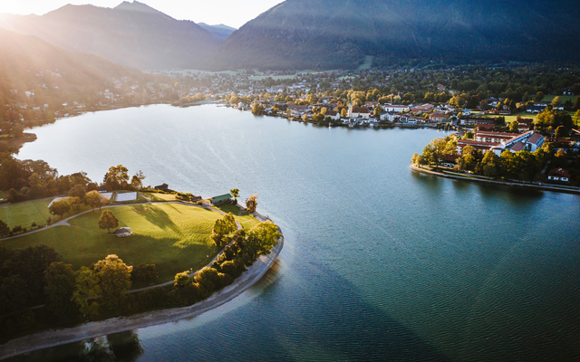 Luftaufnahme eines Sees mit umliegender Landschaft und Bergen im Hintergrund bei Sonnenuntergang