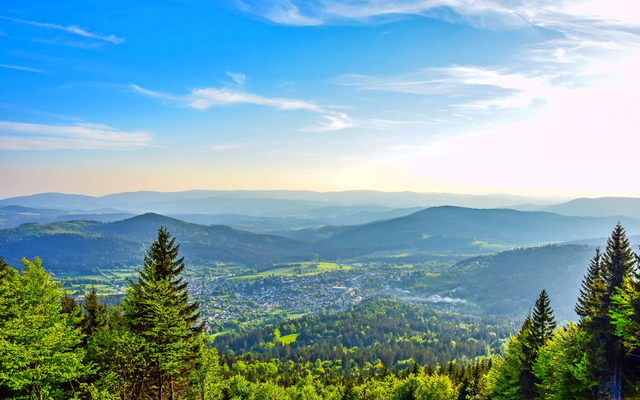 Blick auf eine sonnige Berglandschaft mit Wäldern und einem Tal.