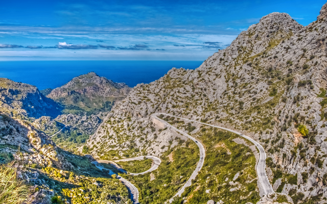 Schlange Straße in bergiger Landschaft mit Meer im Hintergrund.