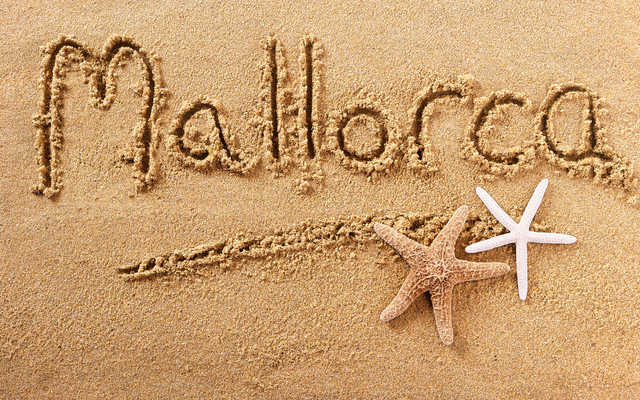 Mallorca im Sand geschrieben auf einem Strand mit zwei Seesternen.