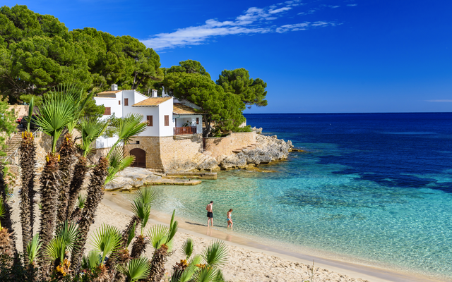 Haus am Strand mit türkisfarbenem Wasser und Pinien im Hintergrund.
