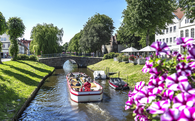 Boot auf einem Kanal in einer grünen Parklandschaft mit Brücke und Blumen im Vordergrund