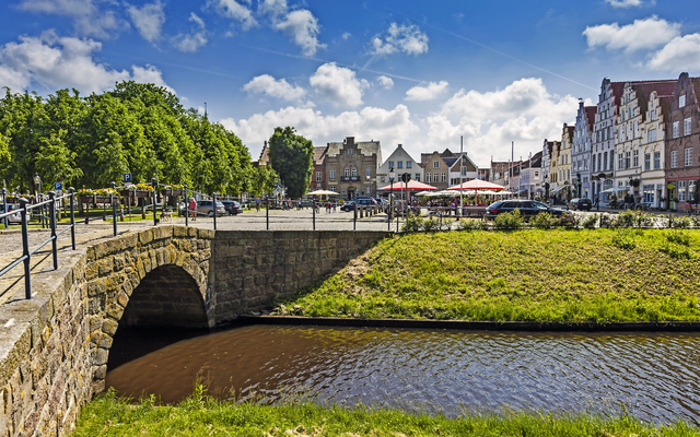Historisches Stadtzentrum mit Fluss und alter Steinbrücke an einem sonnigen Tag.