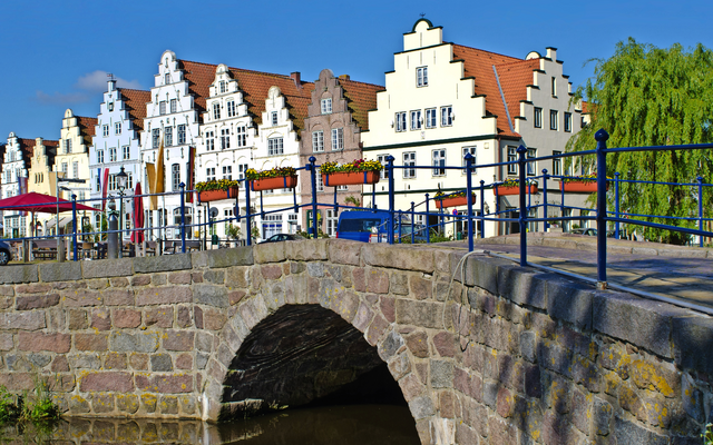 Historischer Gebäudekomplex mit Giebeln hinter Steinbrücke und Wasser.