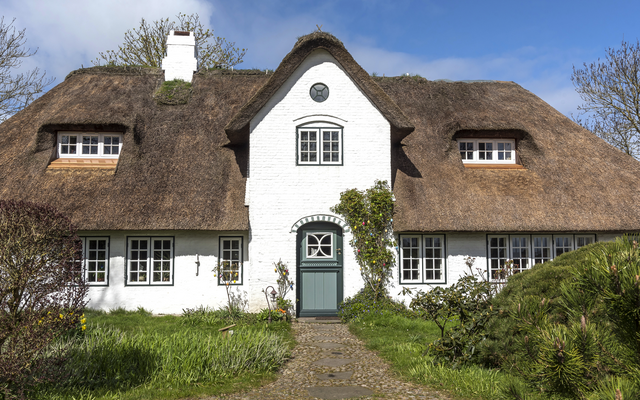 Reetgedecktes Fachwerkhaus mit weißer Fassade und grünem Garten.
