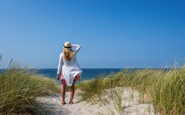 Eine Person am Strand mit Hut, die auf das Meer schaut.