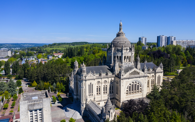 Luftaufnahme einer großen Kathedrale inmitten grüner Umgebung und blauer Himmel.