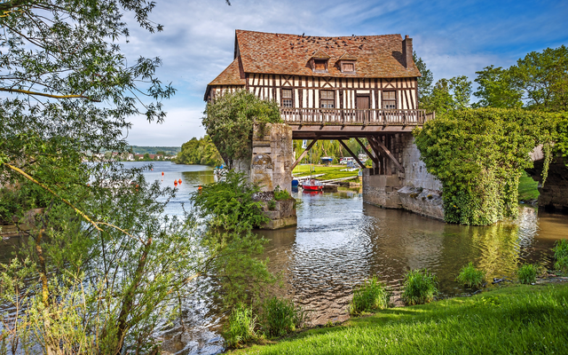 Mittelalterliches Fachwerkhaus auf einer Brücke über einem Fluss, umgeben von Natur.